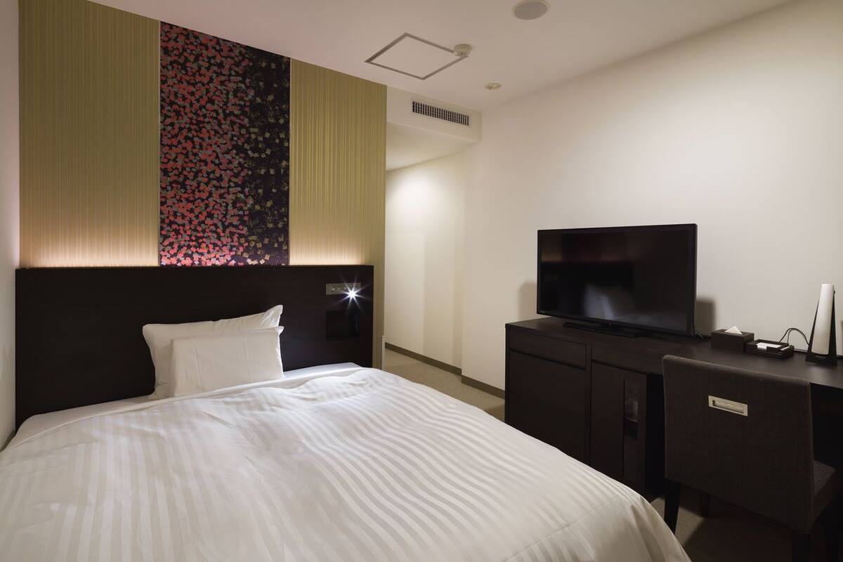 Een hotelkamer met een bed, een televisie op een dressoir, en een bloemenpatroon op de muur.