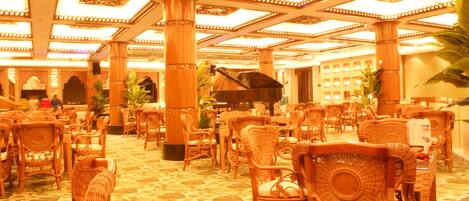 A spacious room with wicker chairs and a grand piano, featuring ornate ceiling designs and a patterned floor.