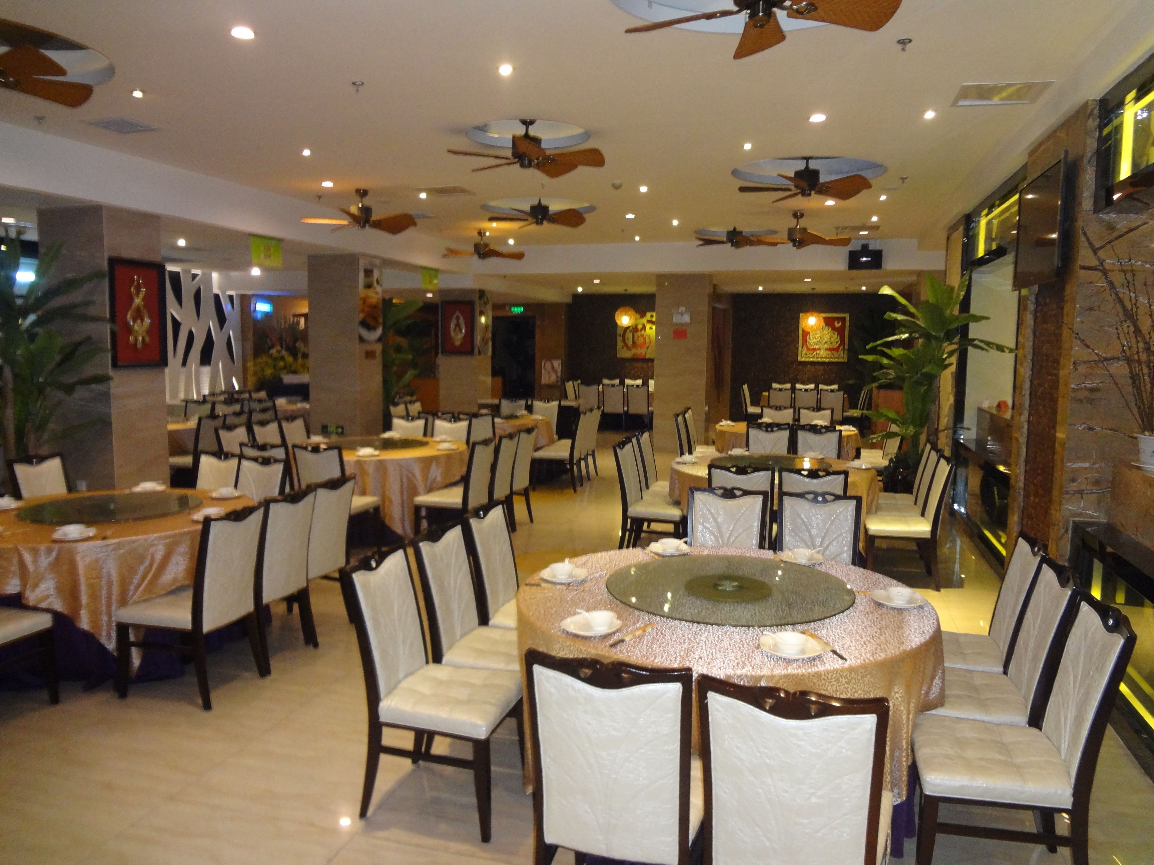 A spacious dining area with multiple round tables, chairs, ceiling fans, and decorative wall elements.