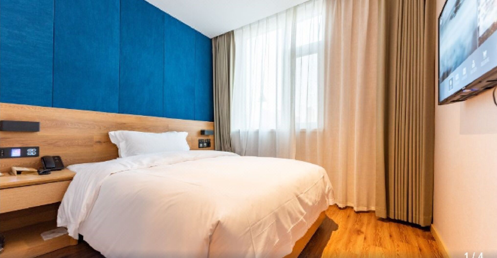 Een hotelkamer met een groot bed, een nachtkastje met een telefoon en een bedieningspaneel aan de muur.