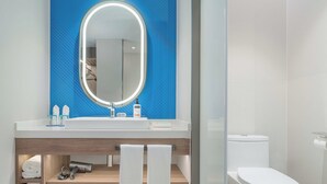A modern bathroom with a blue tiled wall, a round mirror with a light, a white sink, and a toilet. - Holiday Inn Express Wuhan Jinyin Lake by IHG (Wuhan)