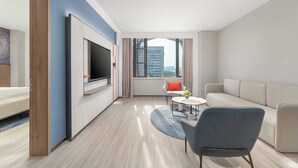 A modern hotel room with a large flat-screen TV, a sofa, a chair, and a small table with a vase of flowers. - Holiday Inn Express Wuhan Jinyin Lake by IHG (Wuhan)