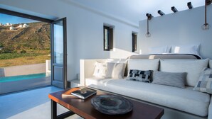 Un salón moderno con un sofá blanco, una mesa de centro y vistas a una piscina y colinas.