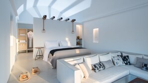 Un dormitorio moderno con cama, sofá y una mesita. Hay estantes con toallas y un jarrón.