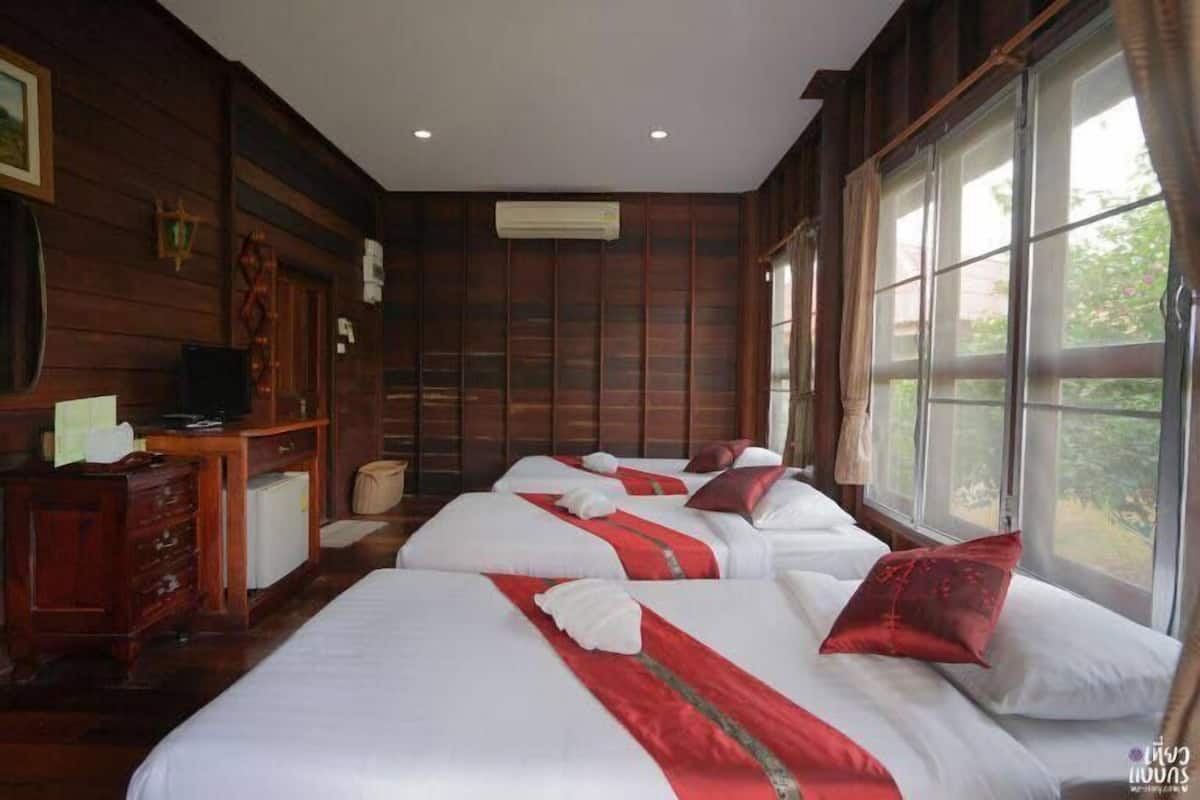 A hotel room with wooden paneling, three beds with red and white bedding, a desk with a television, and large windows.