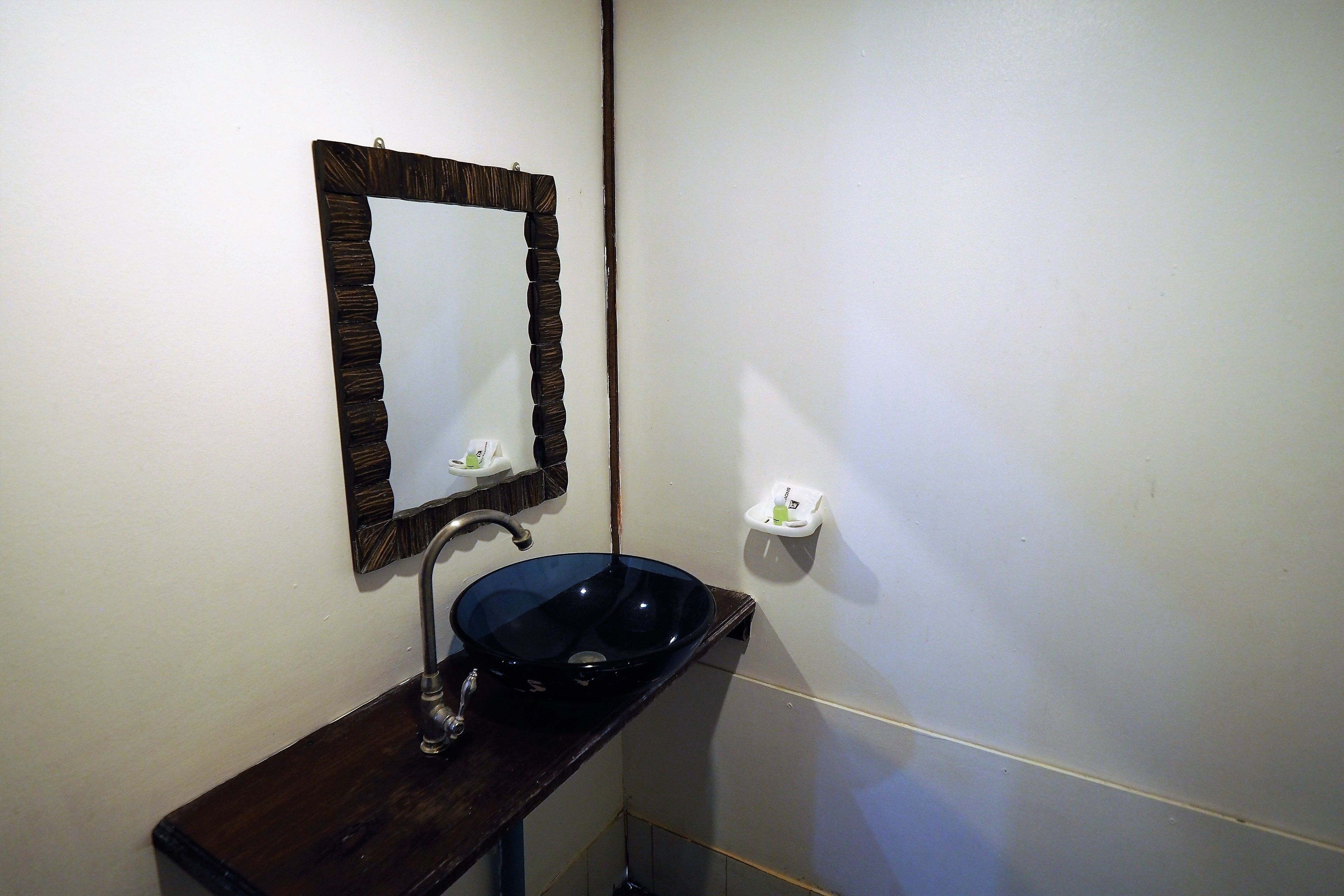 Un baño con tocador de madera oscura, un lavabo negro y un espejo con marco de madera.