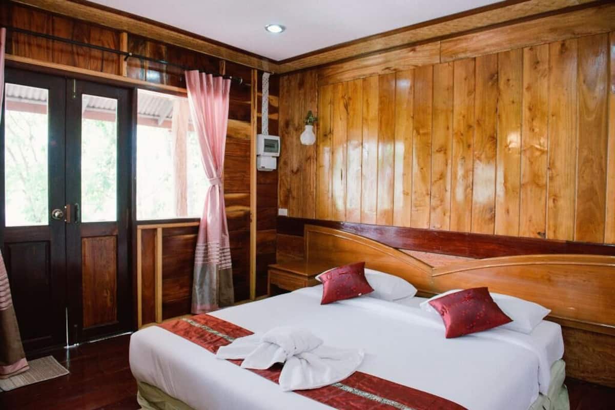 A wooden-paneled room with a bed, curtains, and a thermostat on the wall.