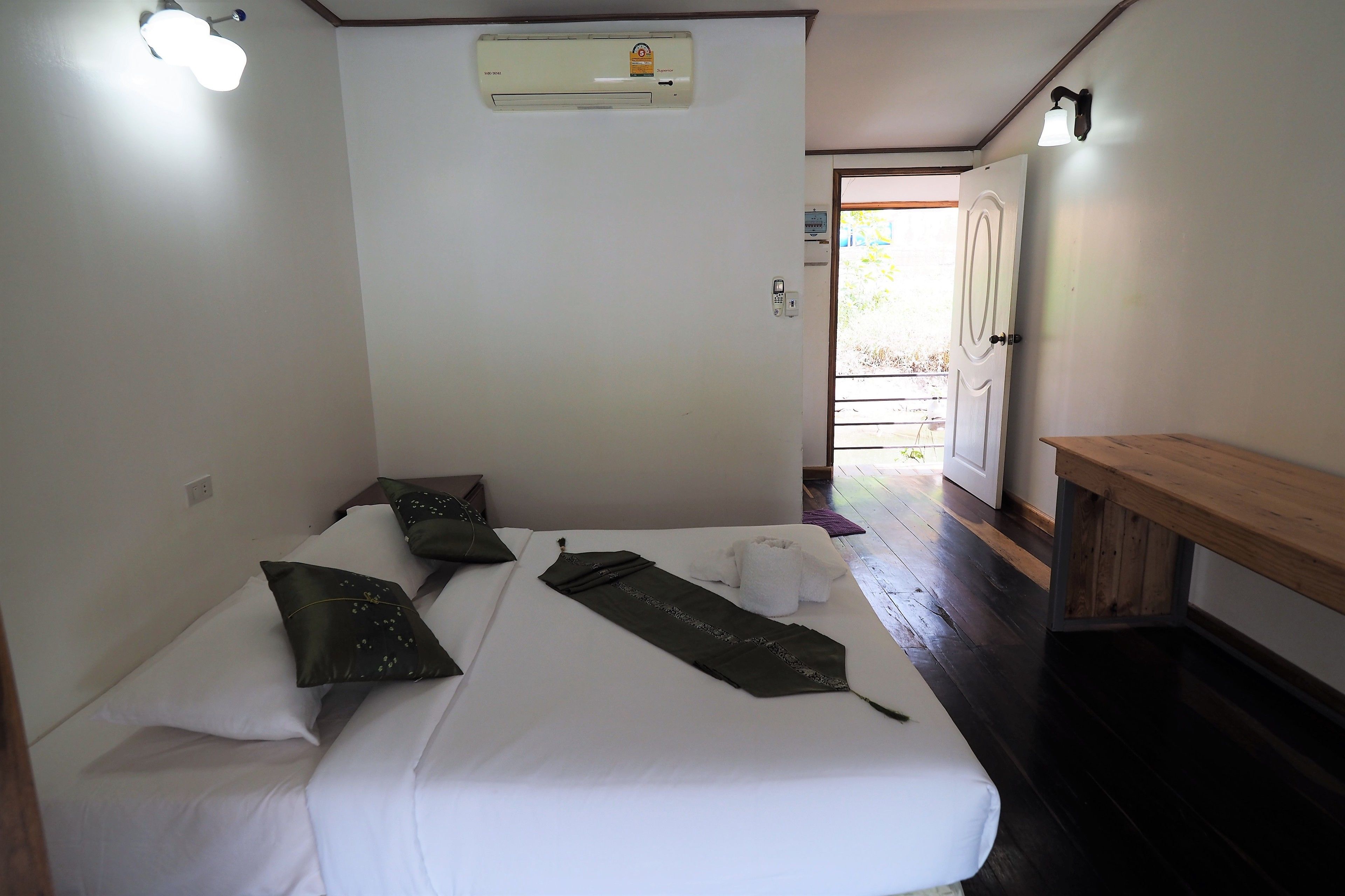 A small, clean room with a bed, a bench, and a door leading to an outdoor area.