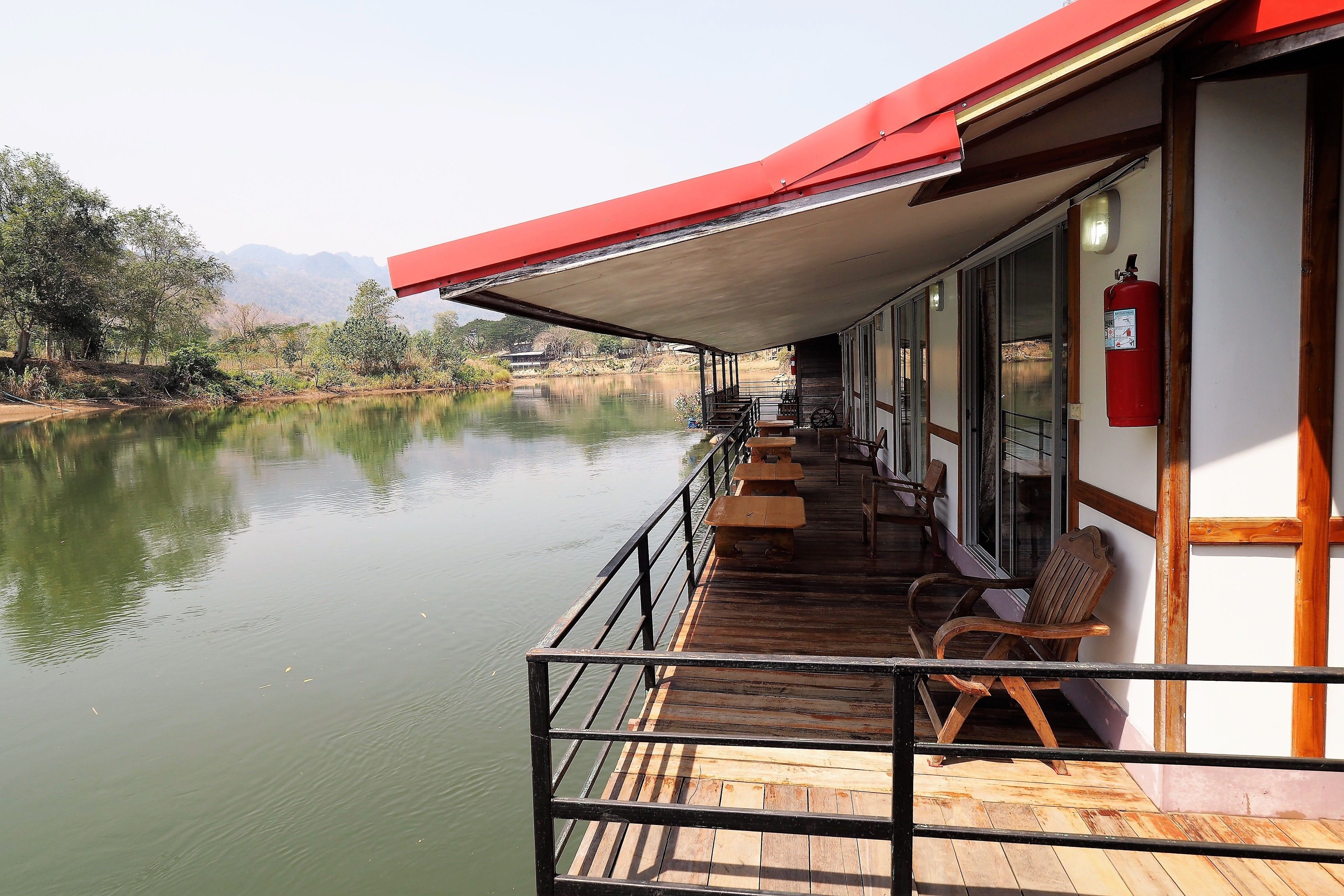 A wooden deck with benches overlooking a calm river, a red awning, and a fire extinguisher on the wall.