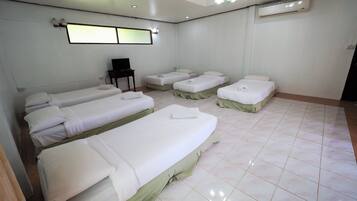 A hotel room with four single beds, a desk with a chair, and an air conditioning unit.