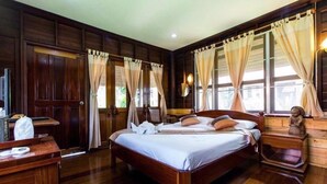 A wooden-floored bedroom with a large bed, curtains, a bedside table, and a nightstand. - Khaothone River View Resort (Sai Yok)