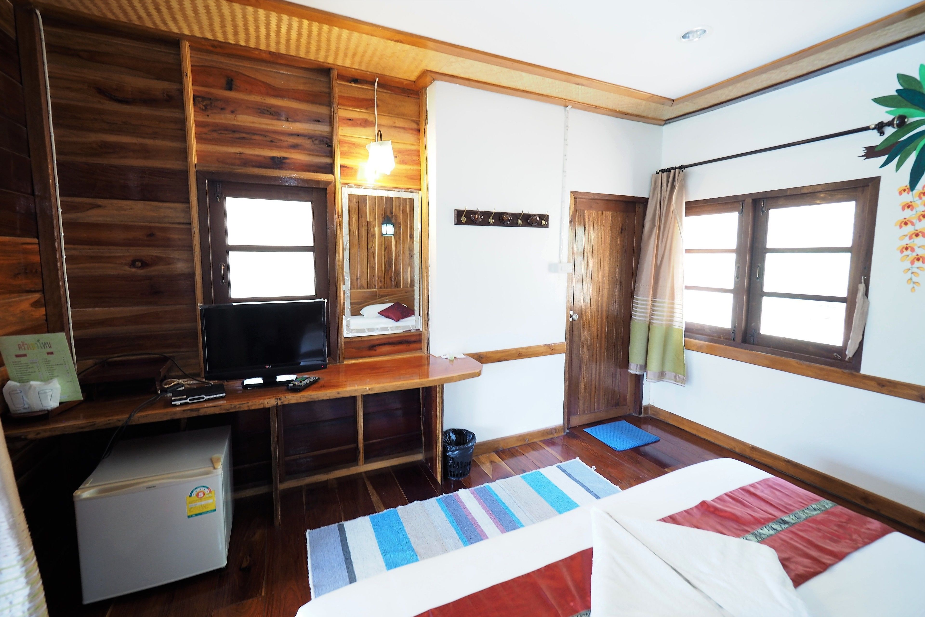 A room with a wooden desk, a television, a bed, and a window with curtains.