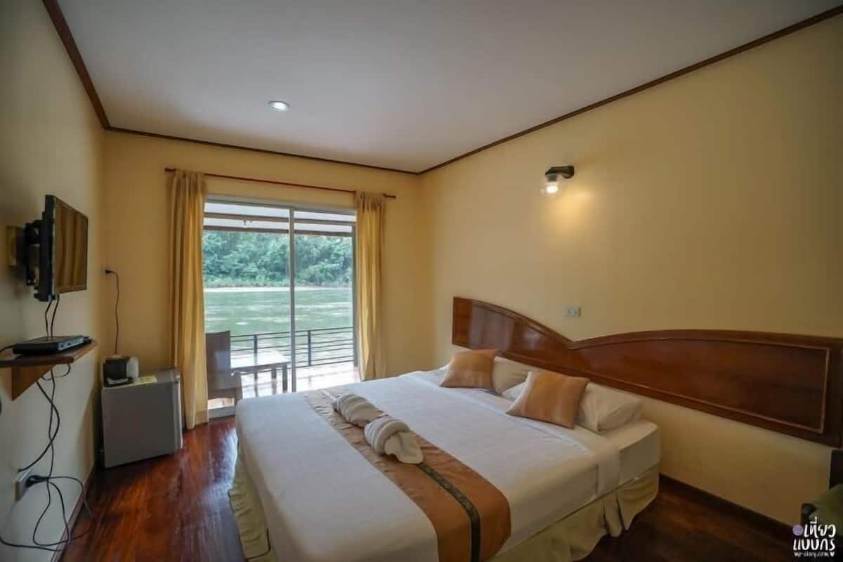 A hotel room with a large bed, a desk with a computer, a TV, and a window with curtains.