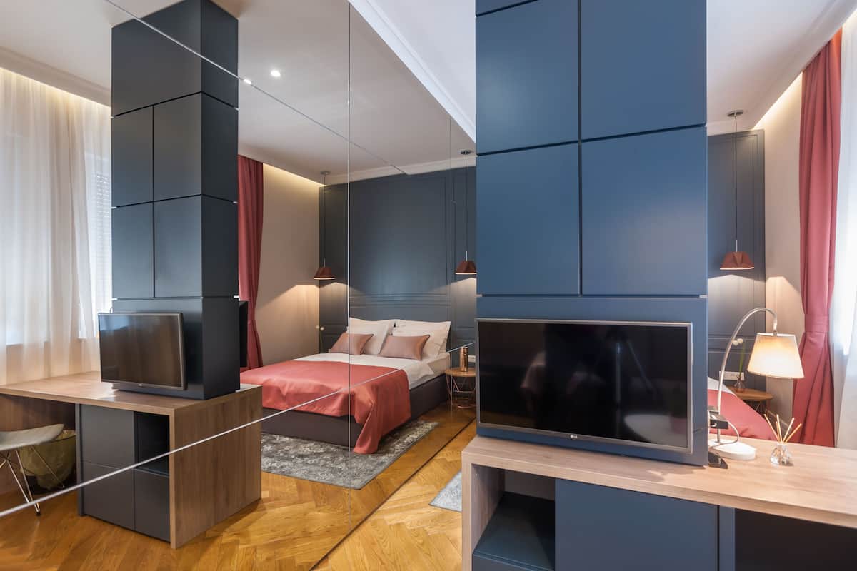 A modern hotel room with a bed, a desk, a TV, and a lamp.