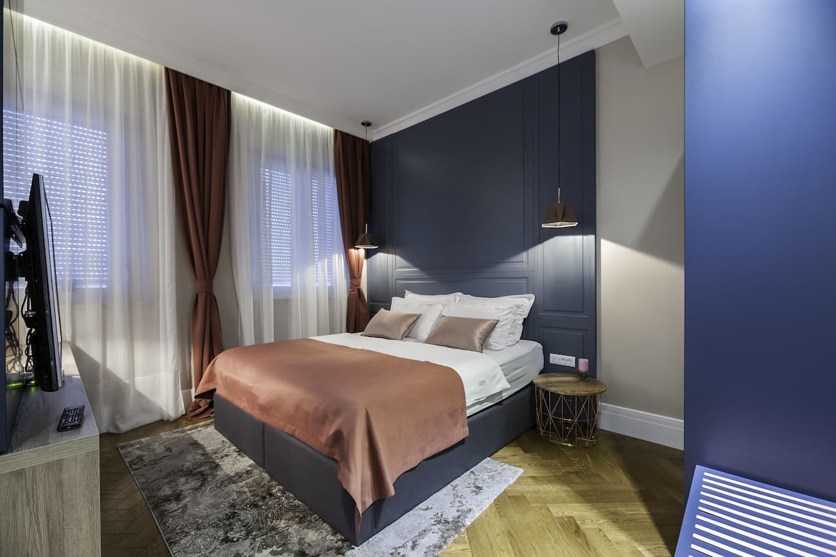 A modern bedroom with a large bed, a bedside table, a lamp, and a view of the outdoors through sheer curtains.