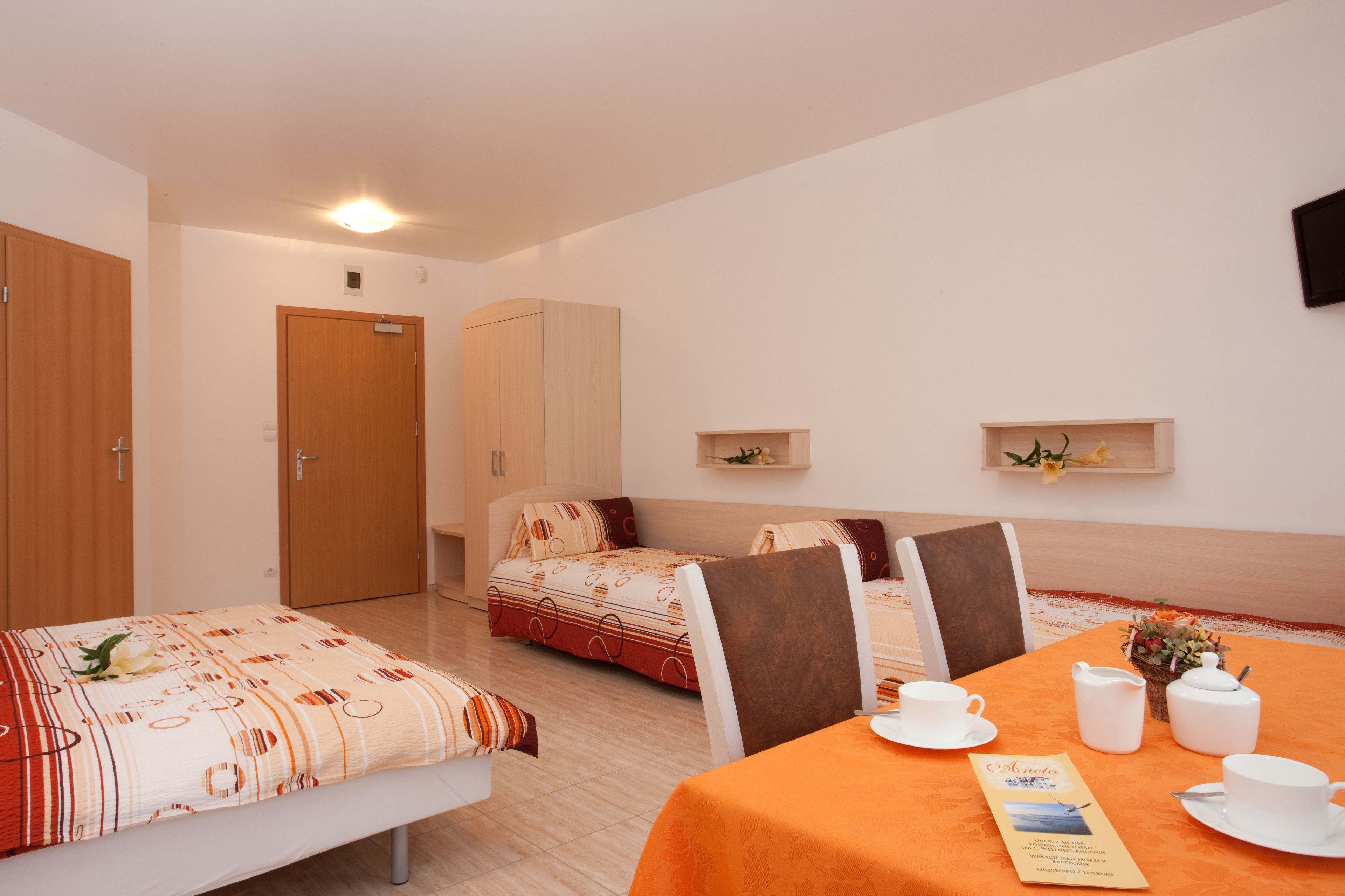 A hotel room with two beds, a dining table set with white tableware, and a small table with a vase of flowers.