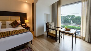 Una habitación de hotel con cama, una silla, una mesa, una lámpara y vistas al exterior.