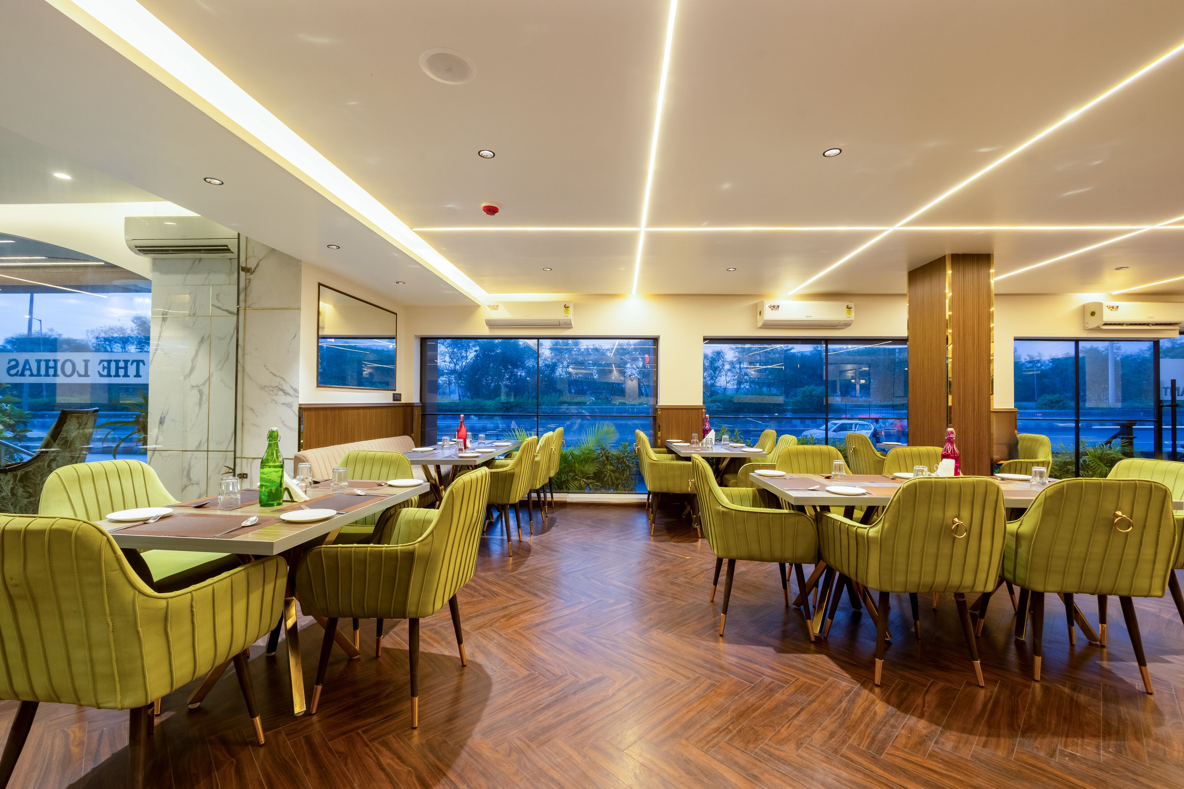 A restaurant with a view of the lake, green upholstered chairs, and a wooden floor.