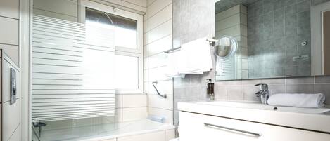 Une salle de bain moderne avec une baignoire, un lavabo, un miroir et une fenêtre avec des stores.