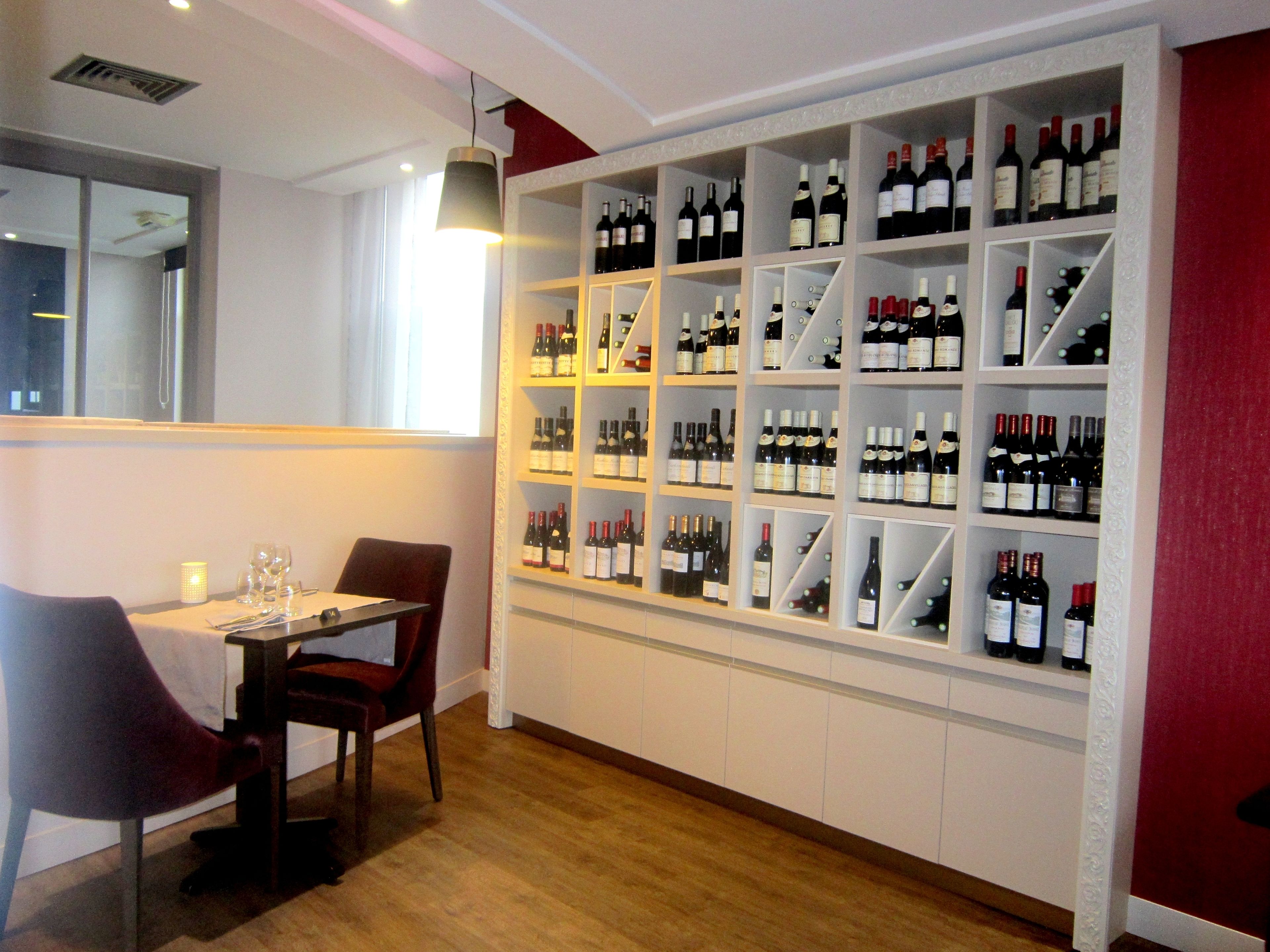 Un coin repas avec une table dressée pour deux personnes, un meuble à vin contenant plusieurs bouteilles et un miroir au mur.