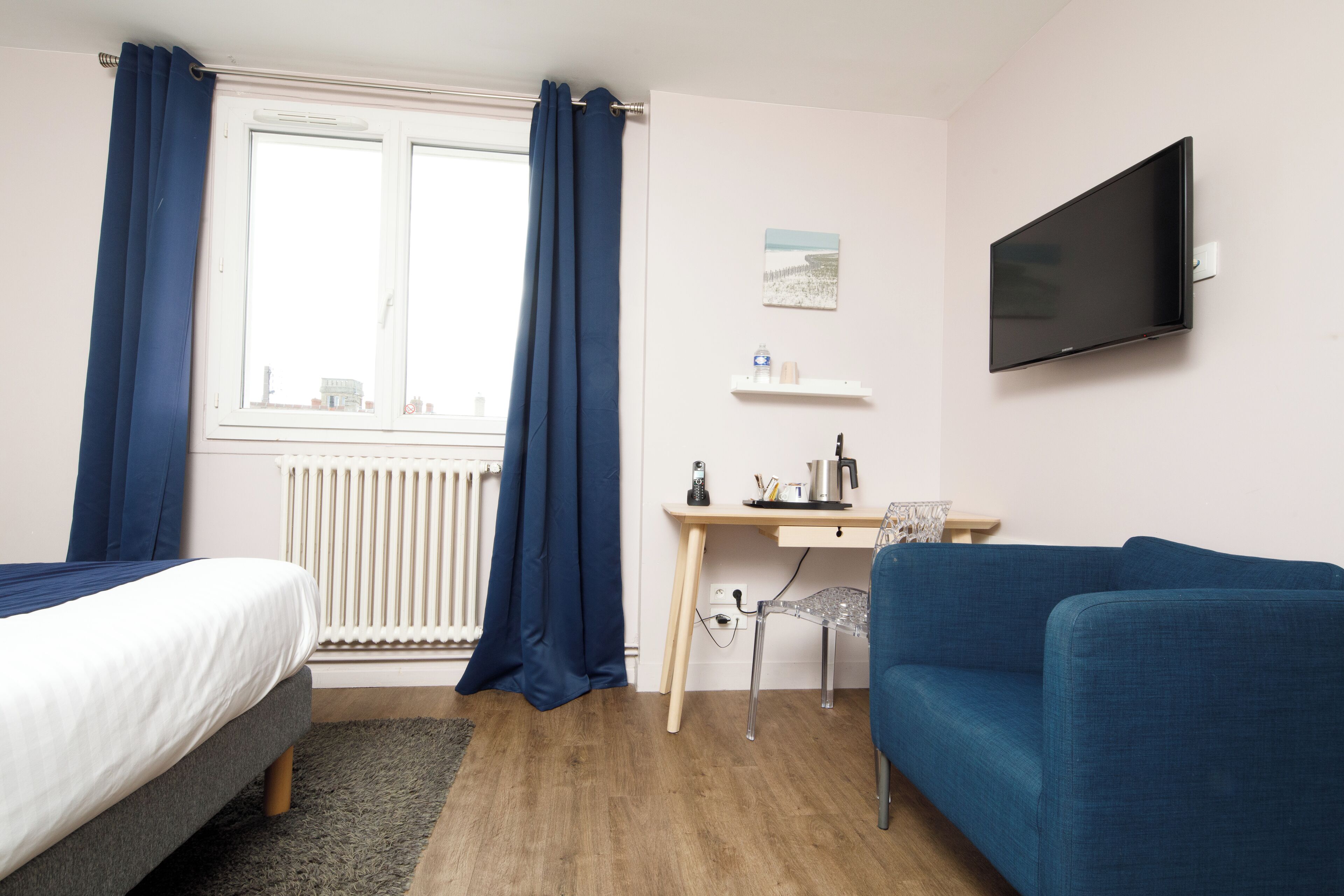 Habitació d'hotel amb llit, escriptori, cadira, sofà blau, televisió i finestra amb cortines.