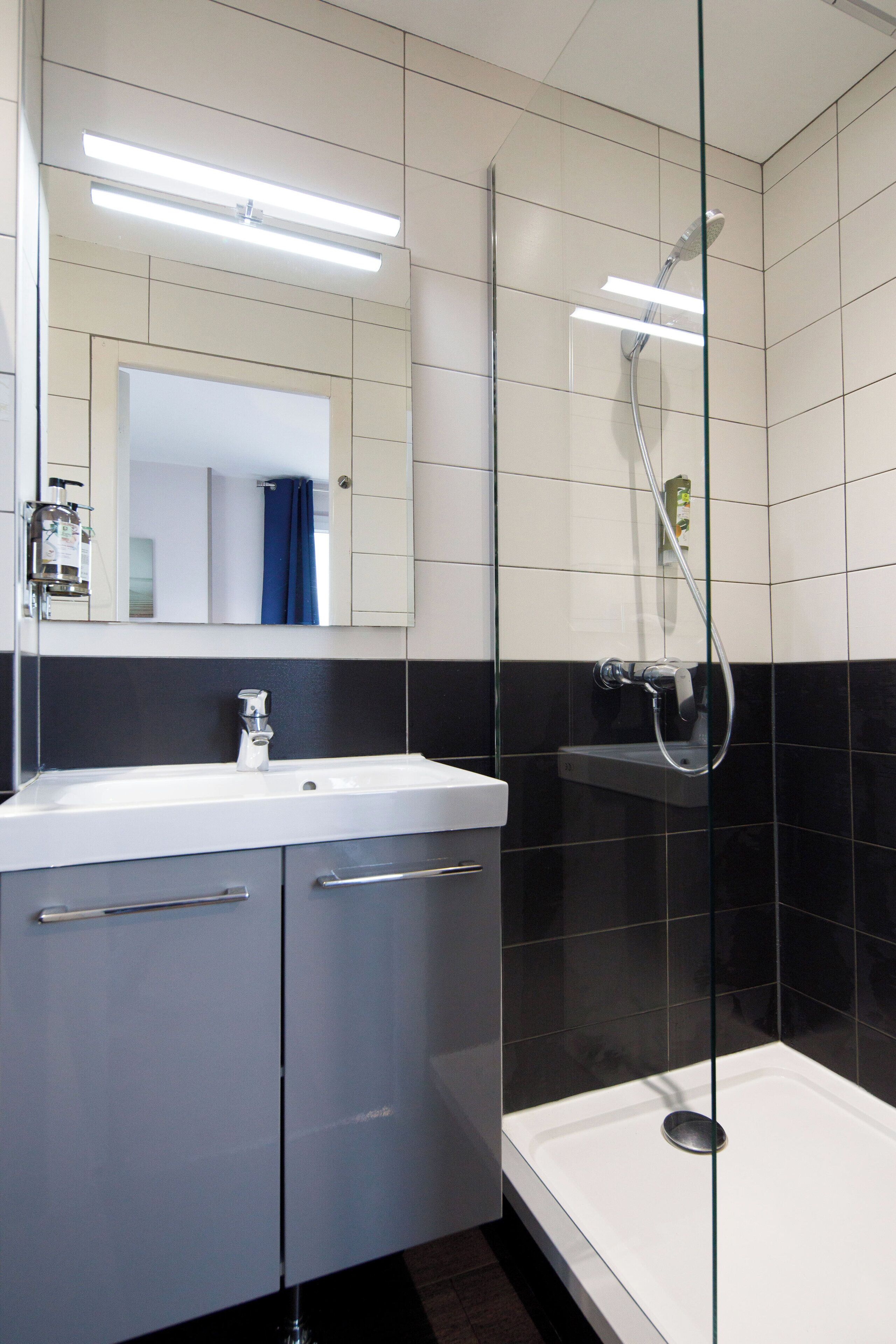 Een moderne badkamer met een douchecabine van glas, een witte wastafel en een spiegel erboven.