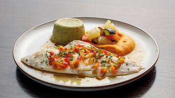 Un plato con un trozo de pescado, una porción de comida verde y un alimento horneado con verduras.