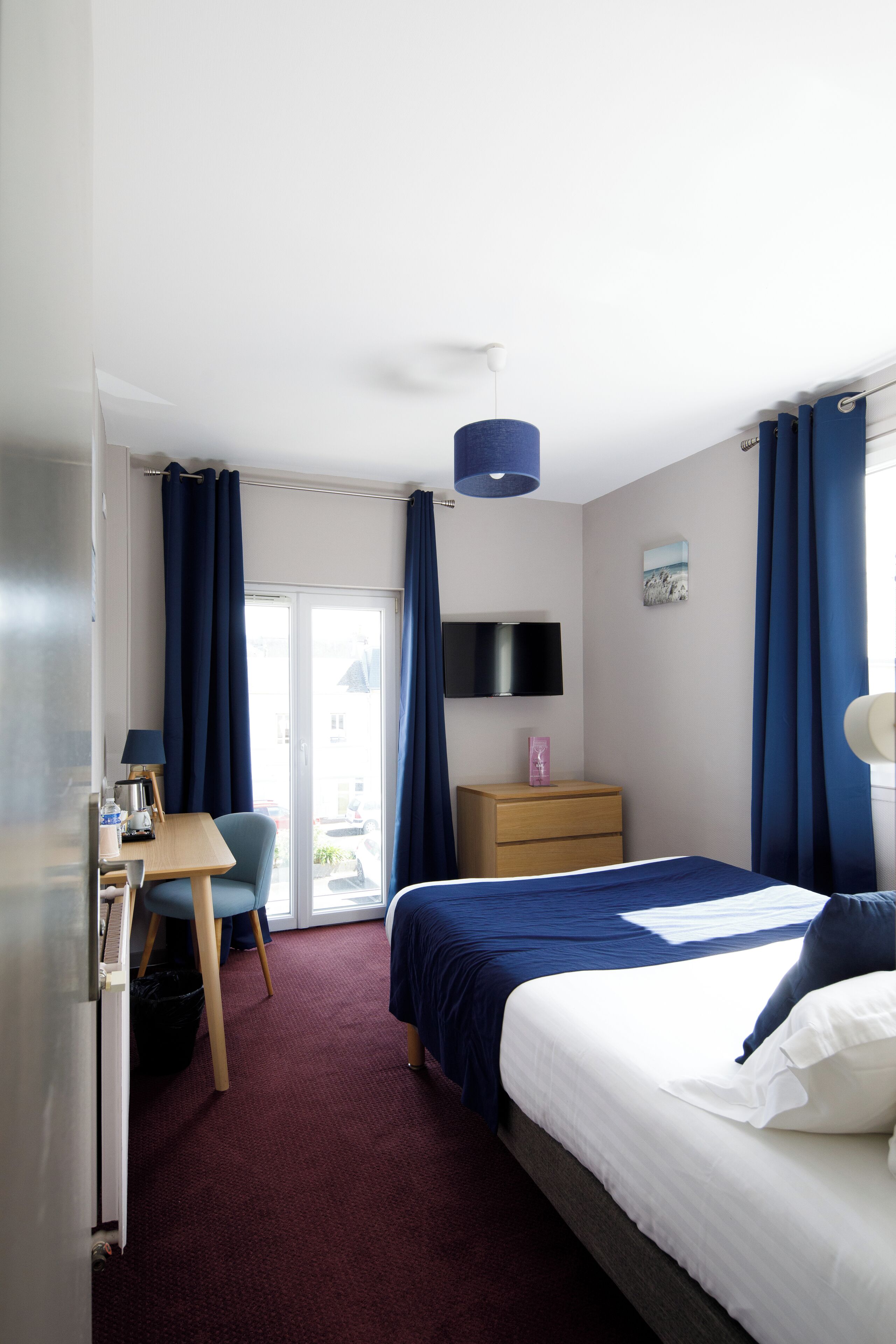 Habitación de hotel con cama, escritorio, silla, televisor y vistas al exterior.