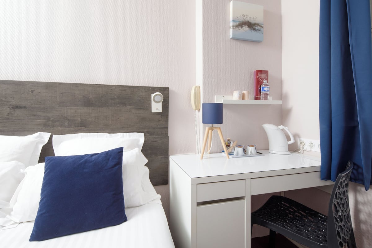 Een hotelkamer met een bed, een bureau, een lamp, een waterkoker en een plank met toiletartikelen.