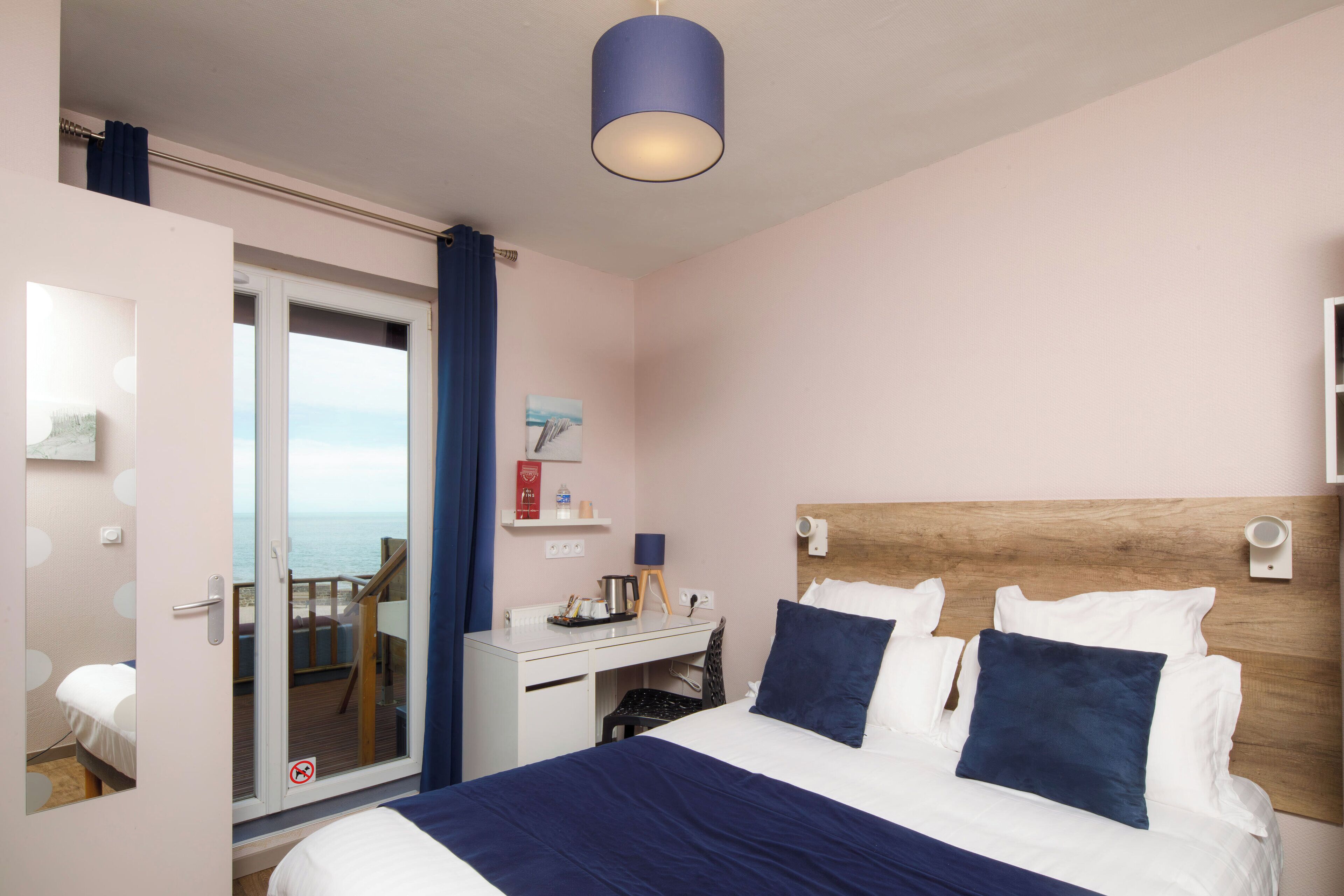 Habitación de hotel con cama, escritorio, silla, vista al mar y una lámpara de techo.
