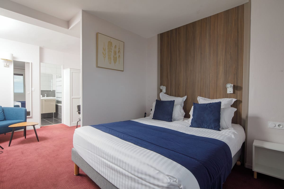 Een moderne hotelkamer met een groot bed, een houten accentmuur, een blauw-witte spreidekker, een tafeltje en een blauwe bank.