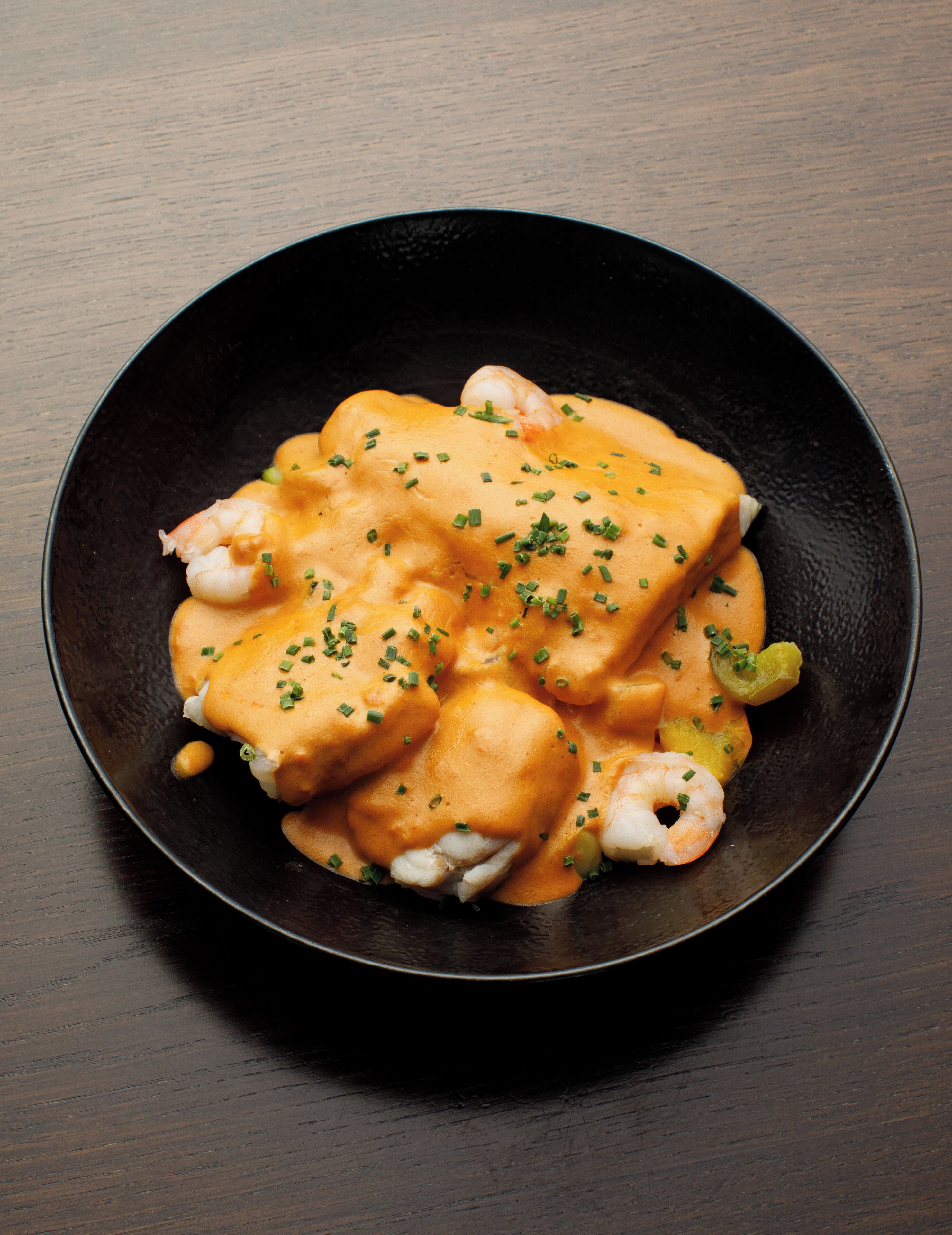 A black plate with a seafood dish, garnished with chives.
