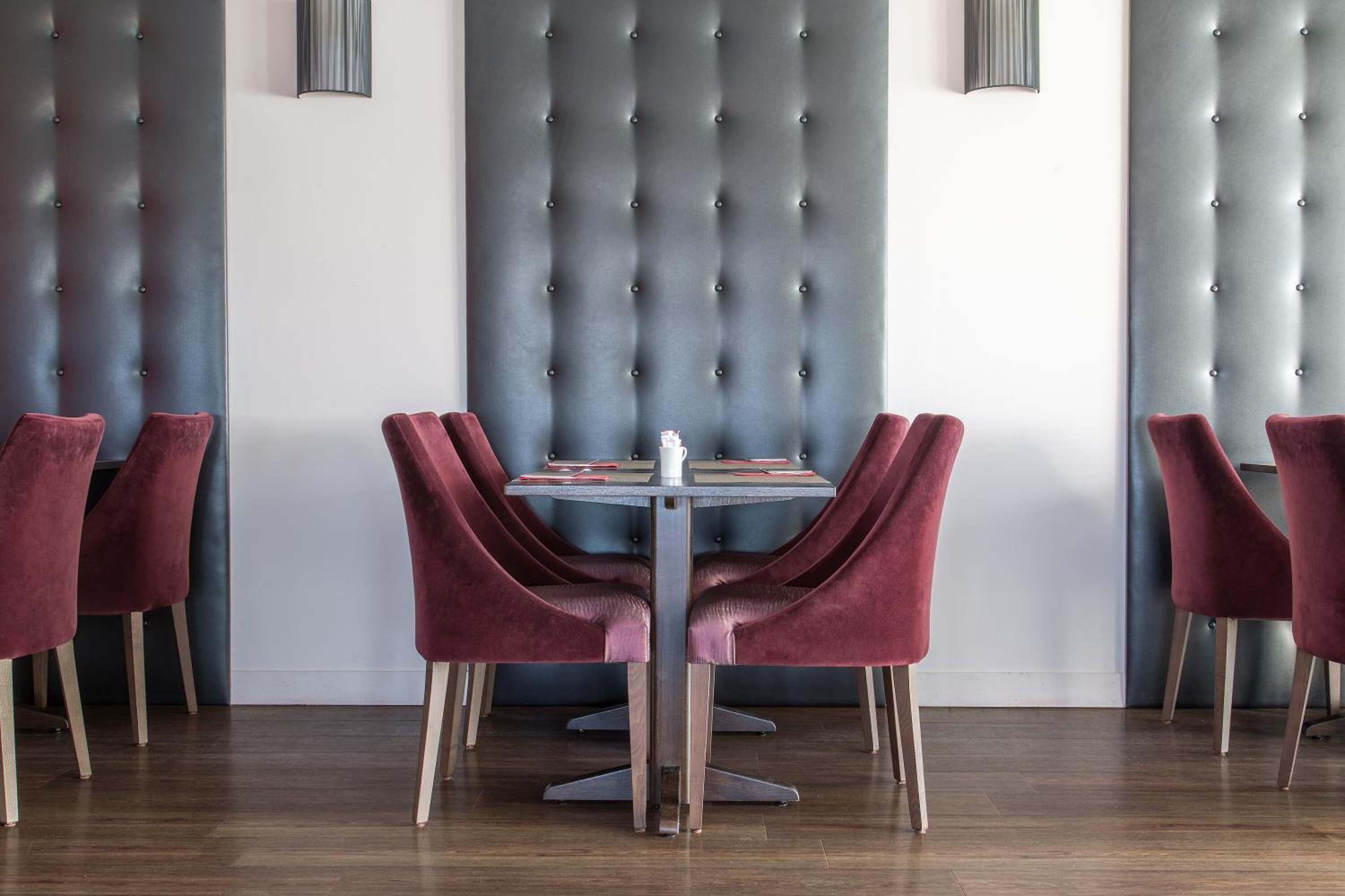 Un comedor con cabecera tapizada, una mesa redonda y seis sillas de terciopelo.