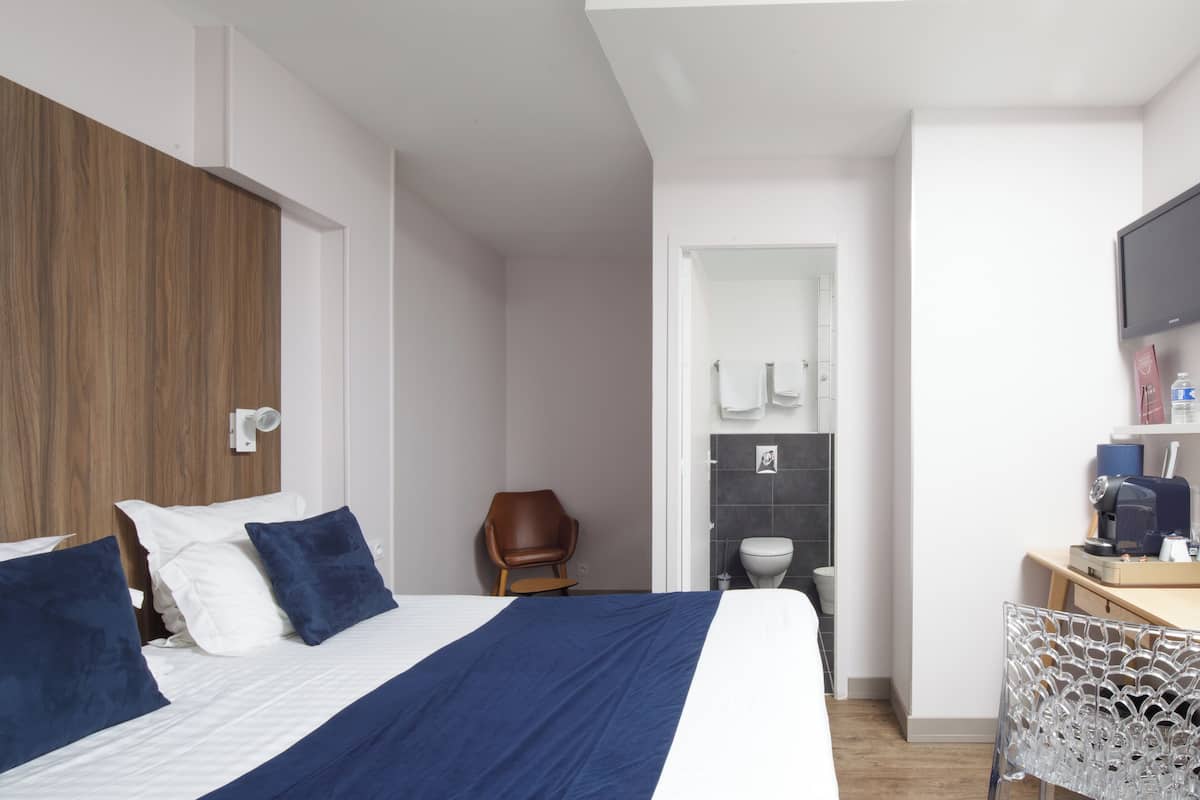 Een moderne hotelkamer met een groot bed, een houten kledingkast, een bureau met stoel, een televisie en een zichtbare badkamer door een geopende deur.