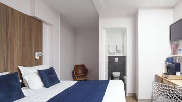 Una habitación de hotel moderna con una cama grande, un armario de madera, un escritorio con una silla, un televisor y un baño visible a través de una puerta abierta.