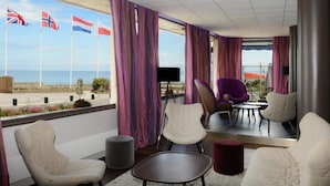 Une chambre d’hôtel avec vue sur la mer, comprenant un coin salon avec des fauteuils et une petite table, un téléviseur à écran plat et des rideaux.