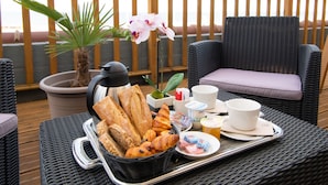 Un plateau de petit-déjeuner avec du pain, des viennoiseries et des produits laitiers, posé sur une table en osier avec vue sur l’océan.