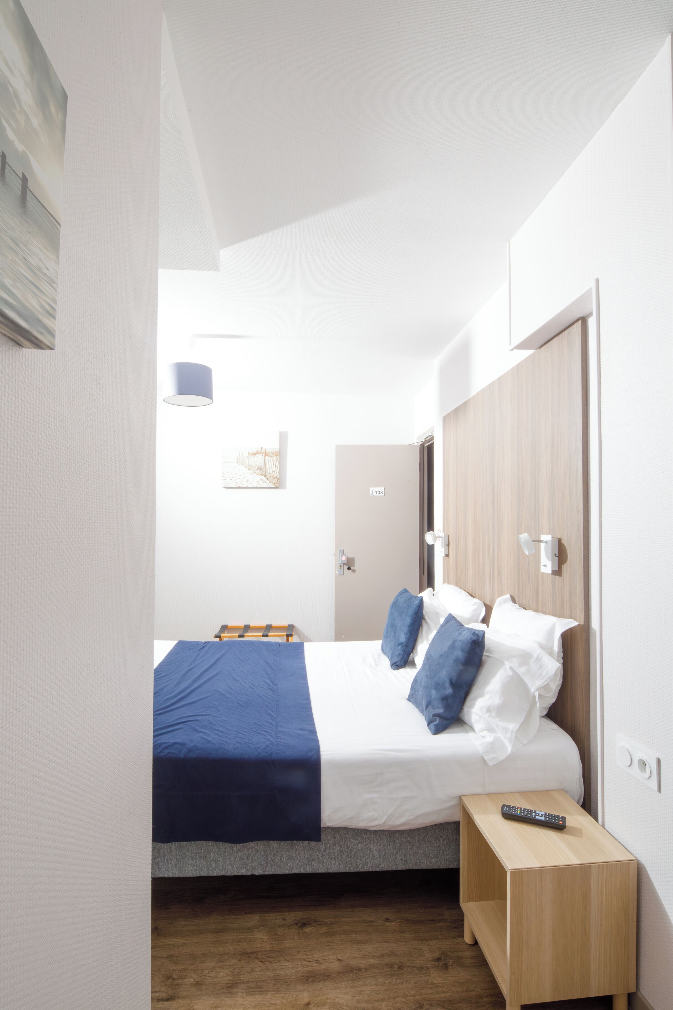 Un dormitorio pequeño y moderno con cama, mesita de noche, control remoto y una puerta.
