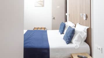 Un dormitorio pequeño y moderno con cama, mesita de noche, control remoto y una puerta.