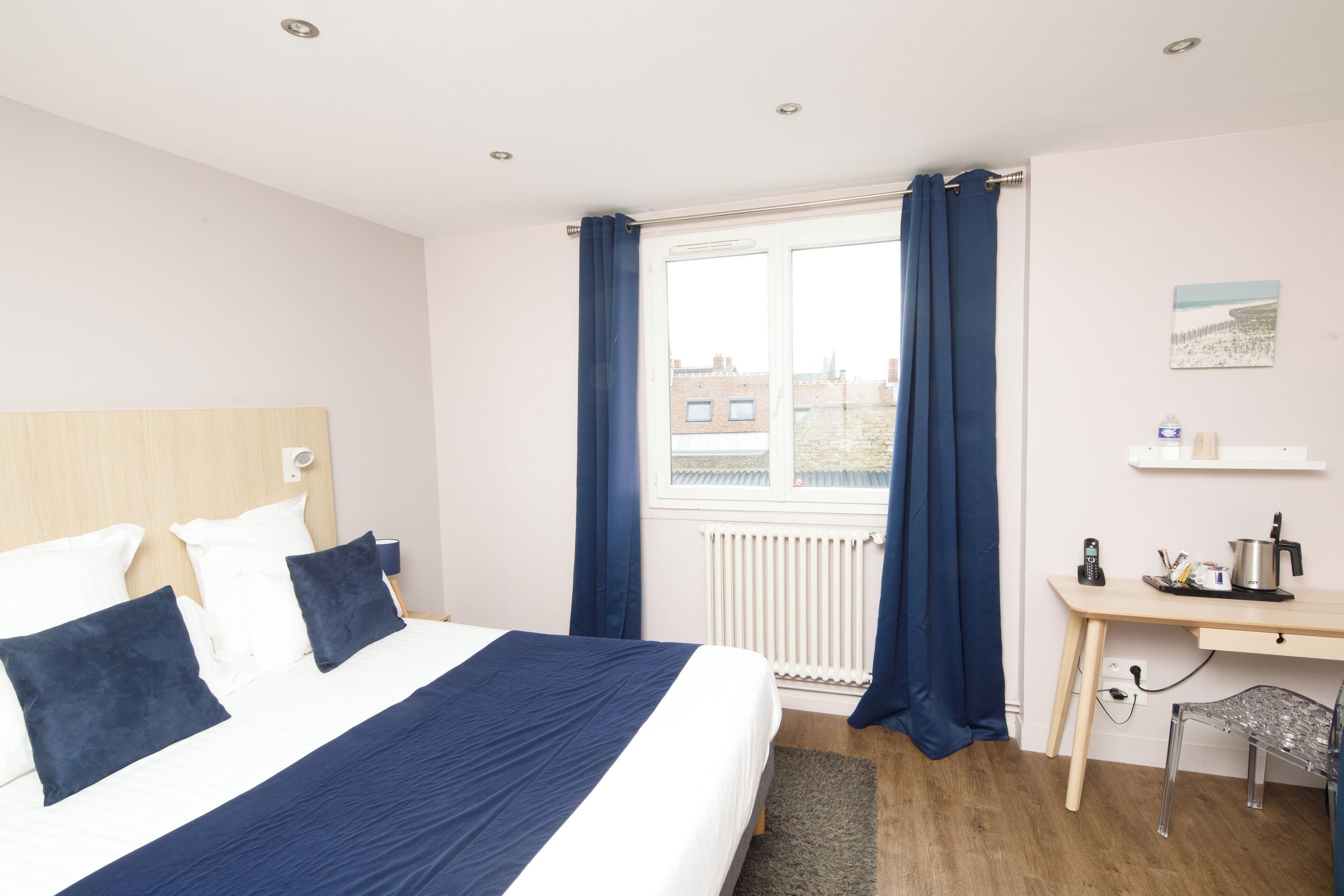 A bedroom with a bed, a desk, and a window with curtains.