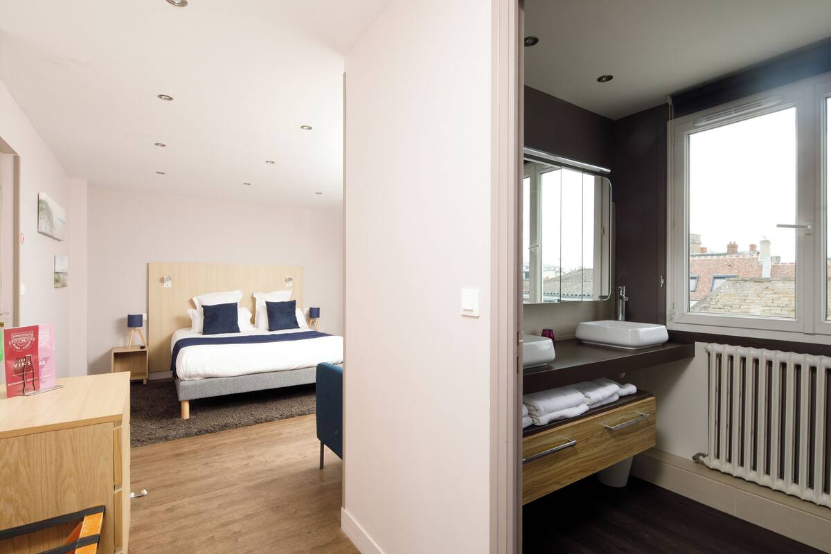 Een moderne hotelkamer met een bed, nachtkastje en uitzicht op de stad door een groot raam.