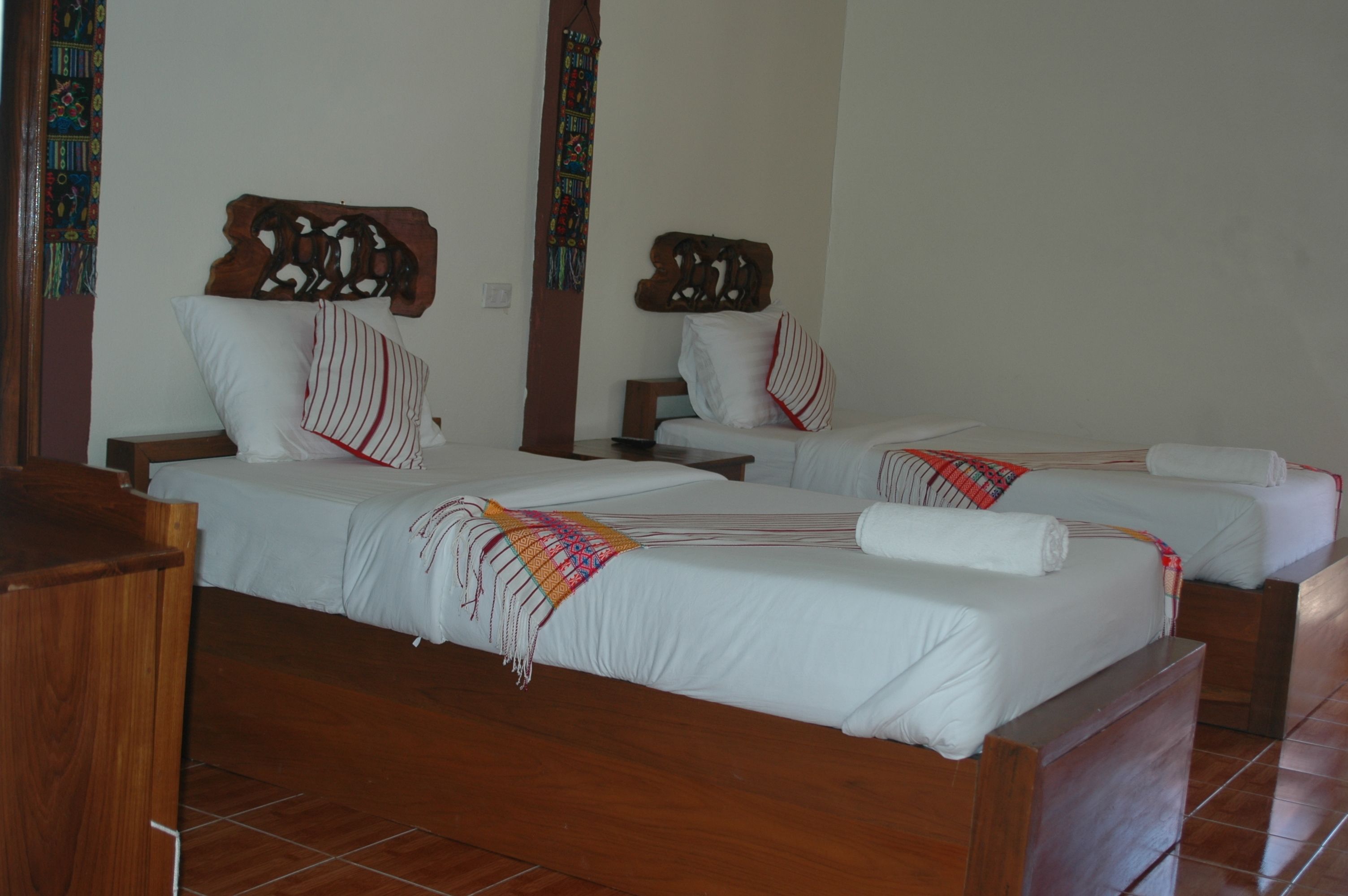 A hotel room with two beds, wooden headboards, white bedding, and a colorful throw blanket.
