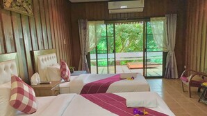 A hotel room with two beds, a large window, and a view of greenery outside.