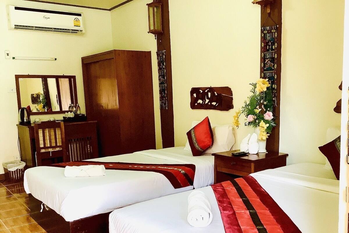 A hotel room with two beds, a wooden wardrobe, a desk with a mirror, and a wall-mounted air conditioner.
