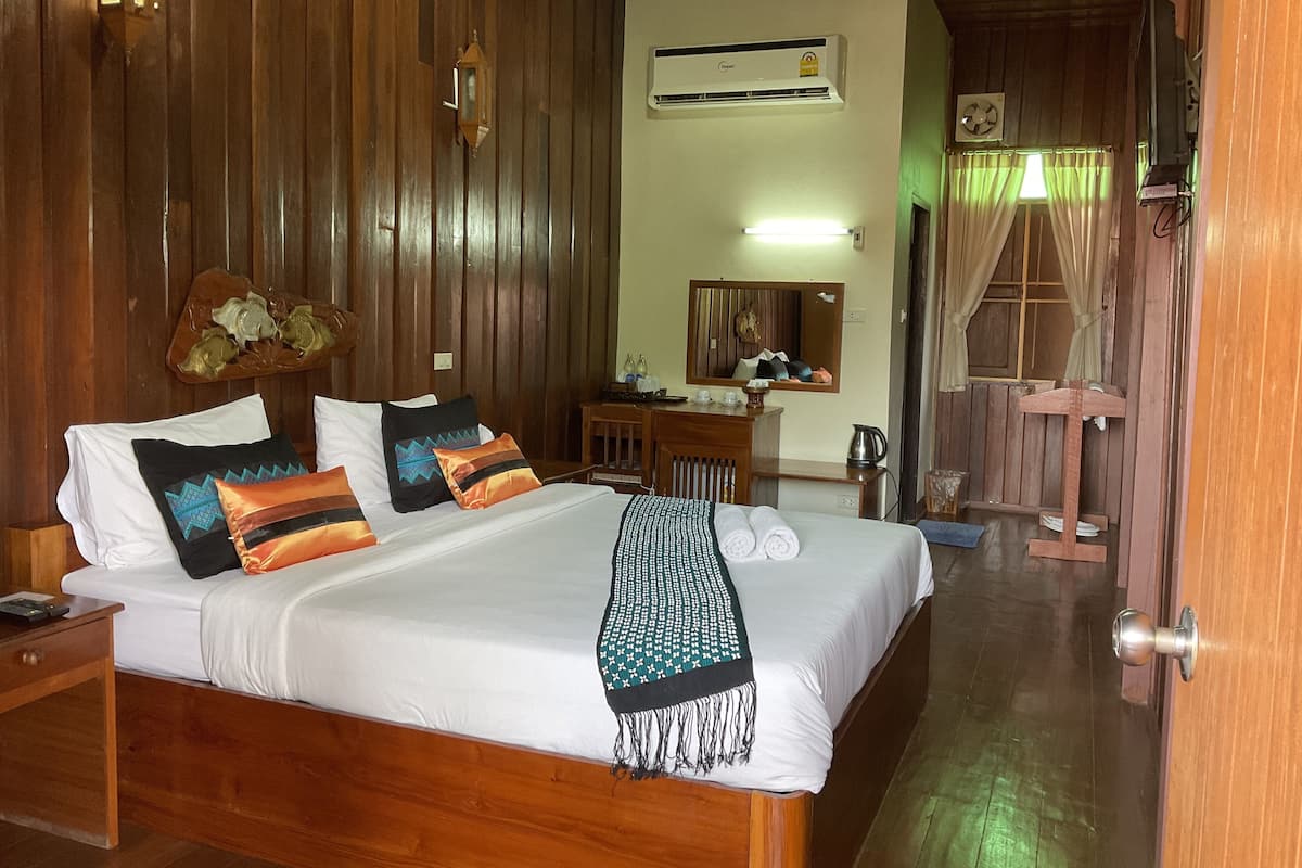 A wooden-paneled room with a bed, a desk, and a mirror.