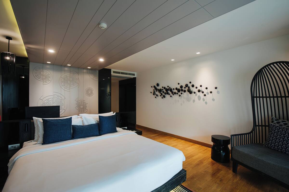 A modern hotel room with a large bed, a seating area, and a wall with decorative patterns.