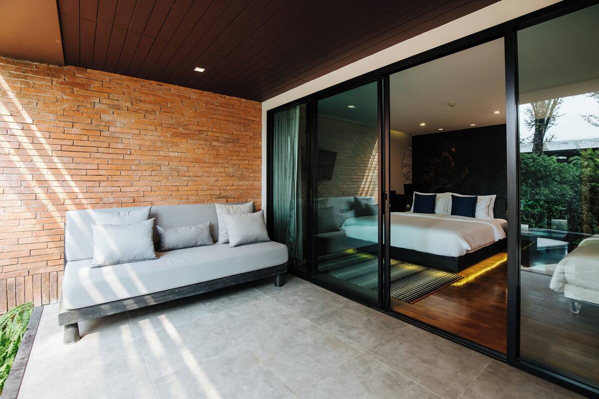 A modern bedroom with a large bed, a sofa, and a sliding glass door leading to a balcony.