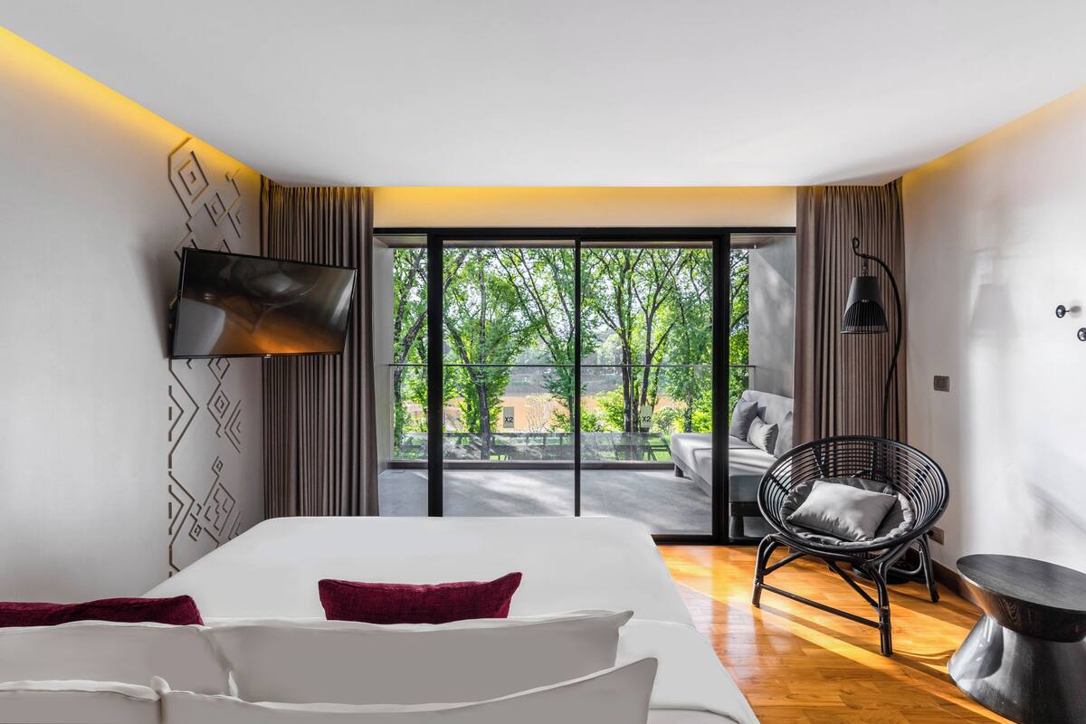 A modern hotel room with a large bed, a flat-screen TV, a comfortable chair, and a dining table.