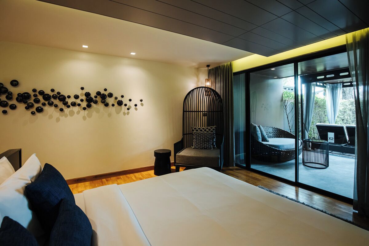 Une chambre d’hôtel moderne dotée d’un grand lit, d’une œuvre d’art murale, d’un fauteuil et offrant une vue sur l’extérieur grâce à une porte-fenêtre coulissante.