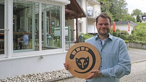 A man holding a wooden sign with a cat symbol.